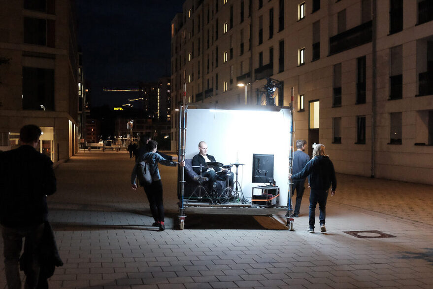 Mehrere Menschen ziehen eine quadratische Bühne durch eine Stadt in der Nacht.