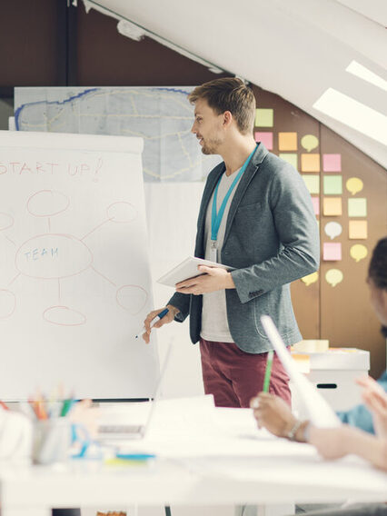 Junger Mann bei schult eine Gruppe anderer Menschen, er steht an einem Flipchart.