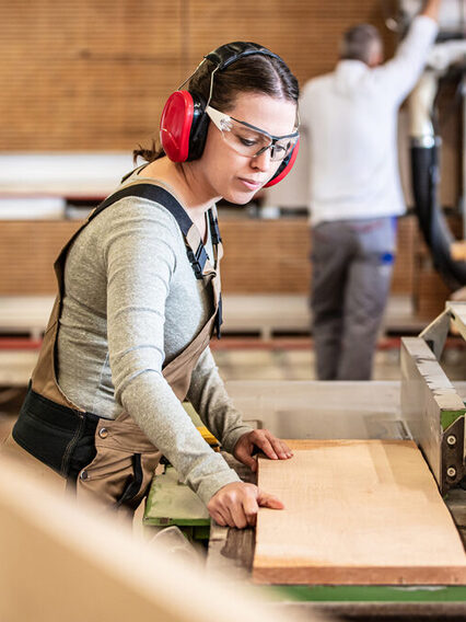 Eine Tischlerin legt ein Holzbrett auf eine Werkbank.