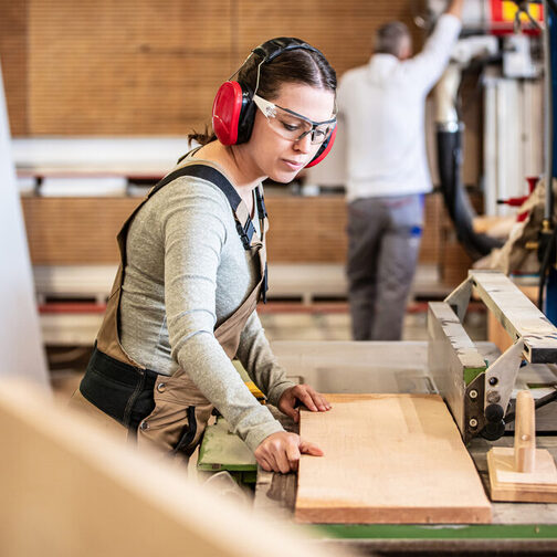 Eine Tischlerin legt ein Holzbrett auf eine Werkbank.