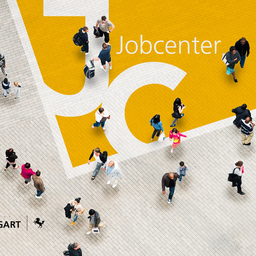 Viele Menschen gehen über einen gepflasterten Platz, das Bild ist aus der Vogelperspektive zu sehen. Auf dem Pflasterboden ist die Wortmarke des Jobcenters Stuttgart zu erkennen.