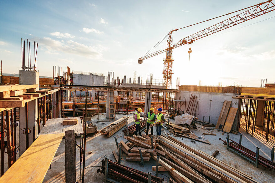 Drei Männer beraten sich auf einer Großbaustelle.