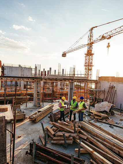 Drei Männer beraten sich auf einer Großbaustelle.