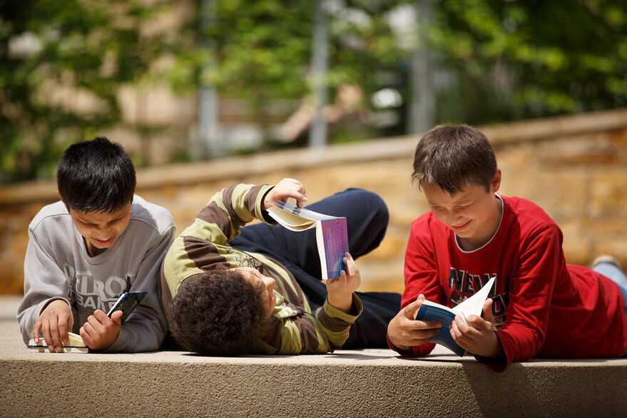 Drei Jungen liegen auf einer Steintreppe und lesen Bücher.