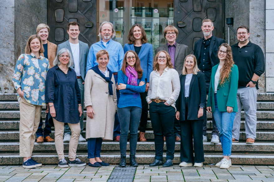 Vierzehn Mitarbeiterinnen und Mitarbeiter des Teams Bildungspartnerschaft stehen in zwei Reihen auf einer Treppe vor einem Eingang.