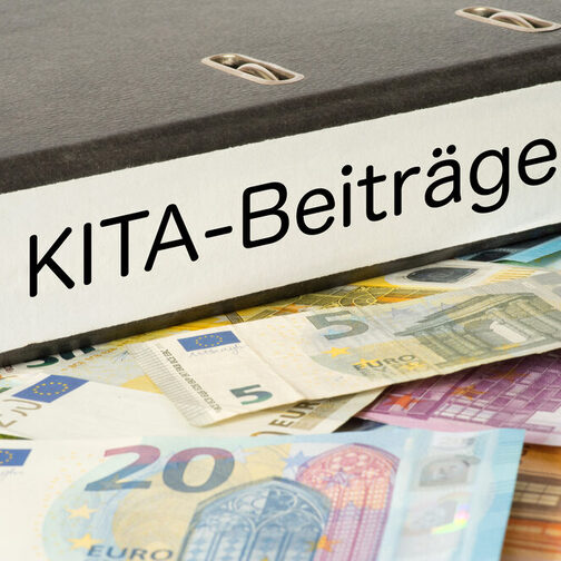 Ein Ordner mit der Aufschrift "Kita-Beiträge" liegt auf Geldscheinen.