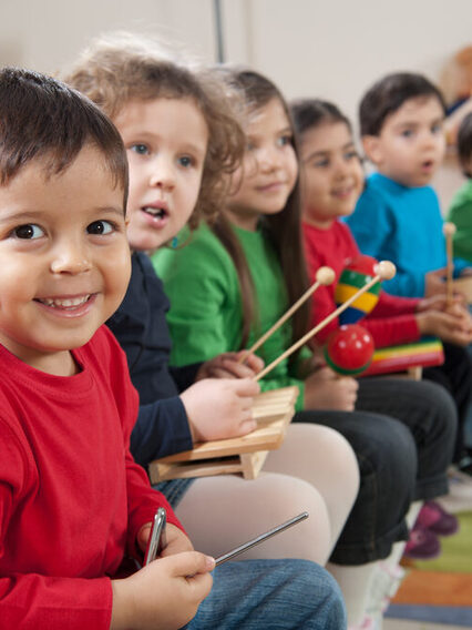 Vorschulkinder sitzen in einer Reihe und halten einfache Instrumente in Händen.