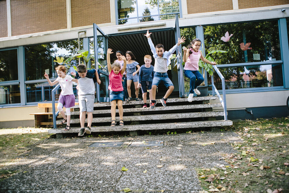 Grundschüler rennen aus dem Schulgebäude in den Schulhof.