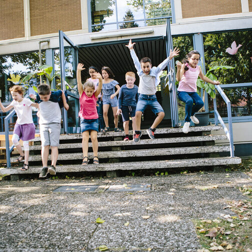 Grundschüler rennen aus dem Schulgebäude in den Schulhof.