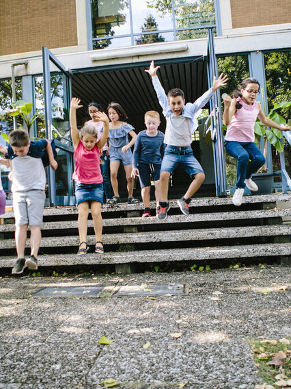 Grundschüler rennen aus dem Schulgebäude in den Schulhof.