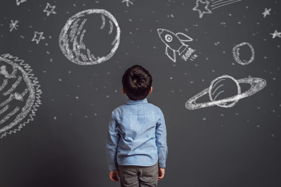 Ein Kind blickt auf eine Tafel mit Kreidezeichnungen von Planeten und Sternen.