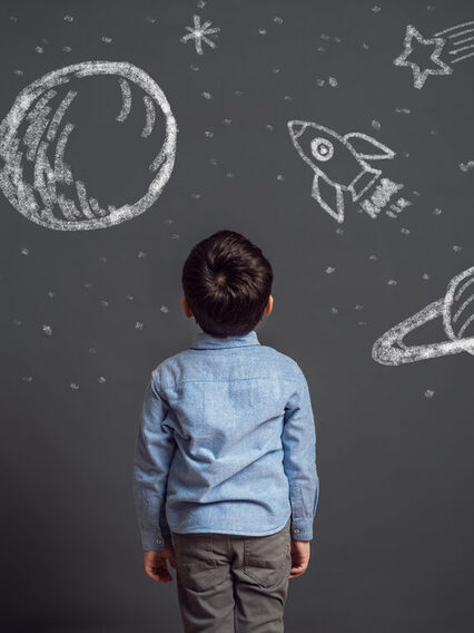 Ein Kind blickt auf eine Tafel mit Kreidezeichnungen von Planeten und Sternen.