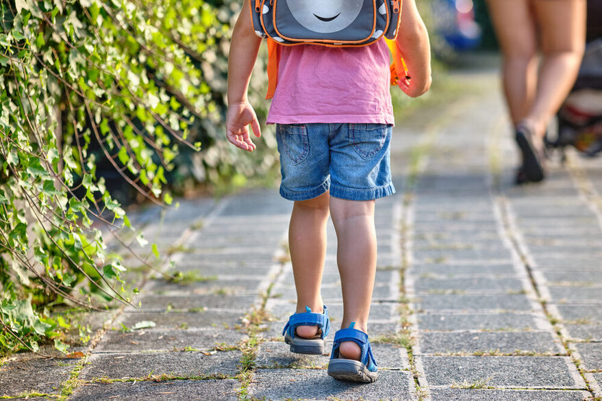 Ein Schulkind ist von hinten zu sehen, mit einem Schulranzen auf dem Rücken.