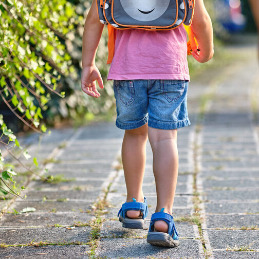 Ein Schulkind ist von hinten zu sehen, mit einem Schulranzen auf dem Rücken.