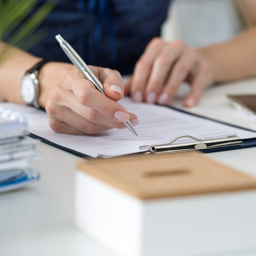 Eine Frau sitzt am Schreibtisch vor einem Blatt Papier und hält einen Stift in der Hand