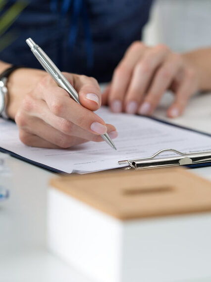 Eine Frau sitzt am Schreibtisch vor einem Blatt Papier und hält einen Stift in der Hand