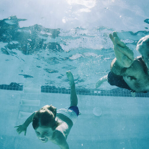 Opa und Enkel tauchen im Schwimmbad bis auf den Grund des Beckens.