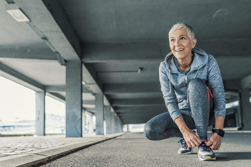 Ältere Dame schnürt sich vor dem Joggen die Schuhe.