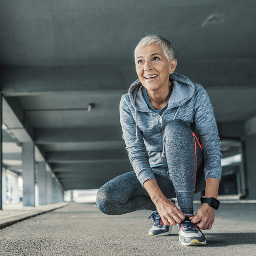 Ältere Dame schnürt sich vor dem Joggen die Schuhe.