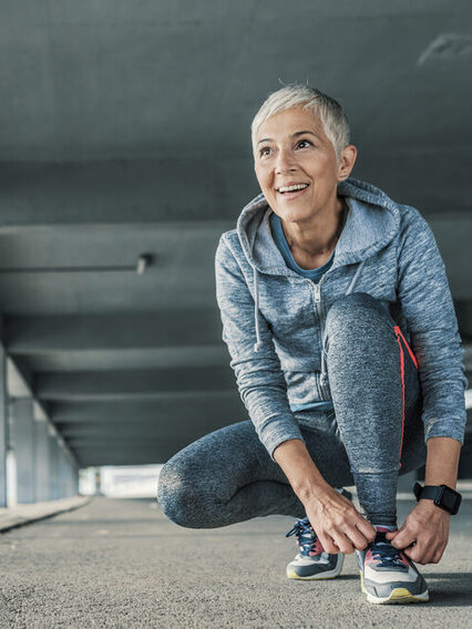 Ältere Dame schnürt sich vor dem Joggen die Schuhe.