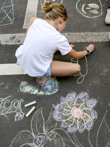 Kinder malen mit bunter Kreide auf einer Straße.