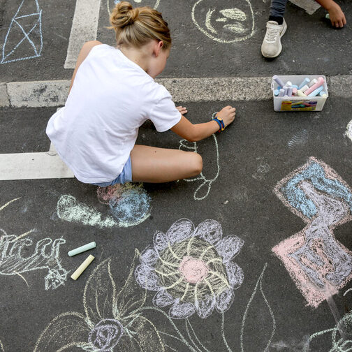 Kinder malen mit bunter Kreide auf einer Straße.