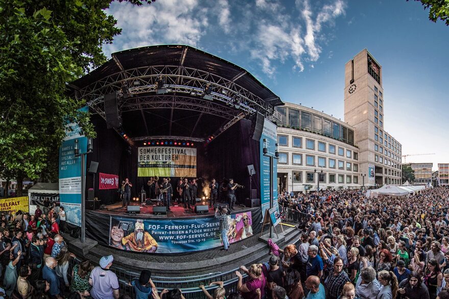 Viele Menschen stehen vor einer Bühne, auf der eine Band auftritt. Im Hintergrund ist das Rathaus zu sehen.