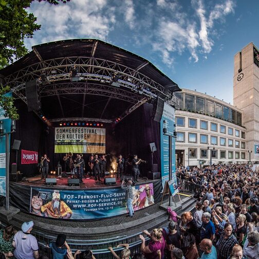 Viele Menschen stehen vor einer Bühne, auf der eine Band auftritt. Im Hintergrund ist das Rathaus zu sehen.