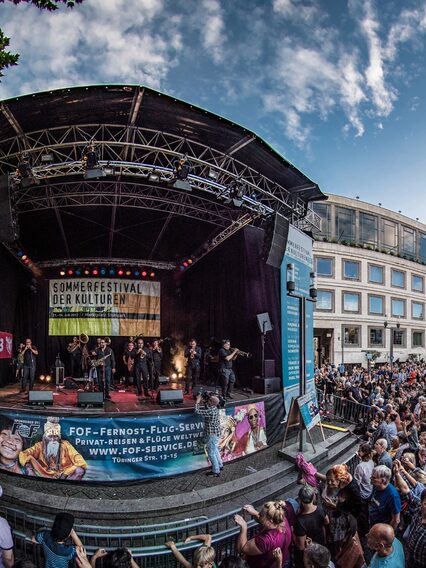 Viele Menschen stehen vor einer Bühne, auf der eine Band auftritt. Im Hintergrund ist das Rathaus zu sehen.