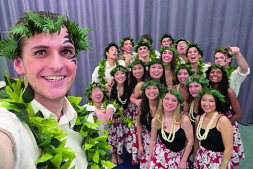 Ein Mann mit Blumenkette im Jahr macht ein Foto von sich und einer Gruppe Menschen.