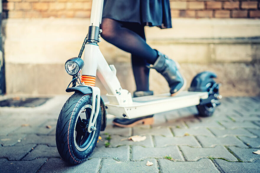 Nahaufnahme vom E-Scooter: Ein Frau steht mit schwarzen Schuhen auf einem E-Scooter.