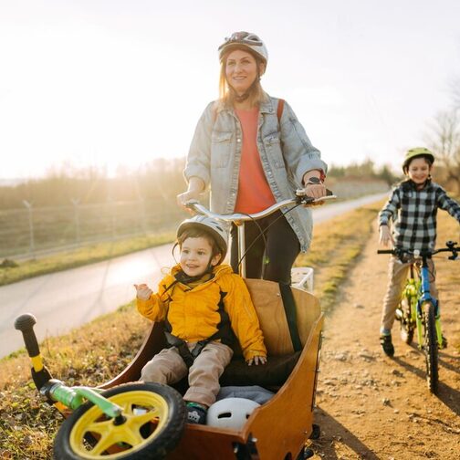 Frau mit Lastenrad mit Kleinkind darin sowie Junge auf Fahrrad