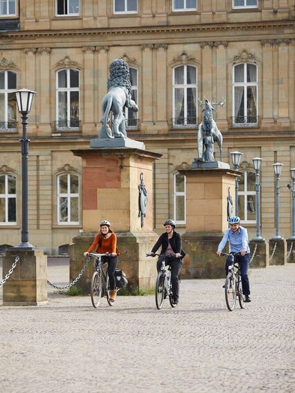 Drei Menschen radeln an einem Schloss vorbei.