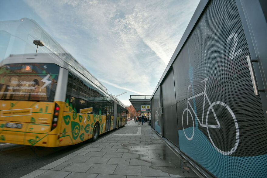 Ein Bus fährt in einer Bushaltestelle ein, auf der rechten Seite befindet sich eine Fahrradgarage.