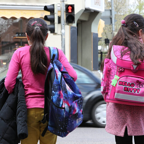 Zwei Mädchen auf dem Weg zur Schule stehen an einer roten Ampel.