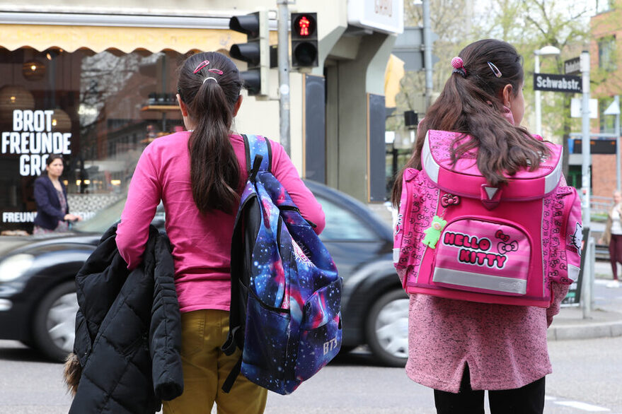 Zwei Mädchen auf dem Weg zur Schule stehen an einer roten Ampel.