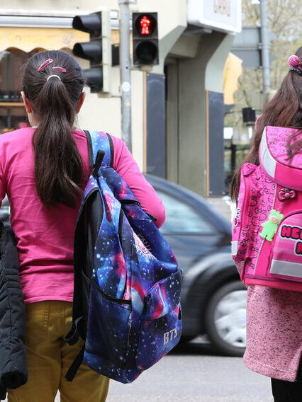 Zwei Mädchen auf dem Weg zur Schule stehen an einer roten Ampel.