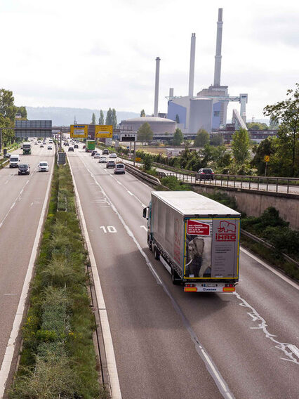 Blick auf eine Bundesstraße mit vielen Autos und Lastwagen. Links im Hintergrund ein große Fabrikhalle.