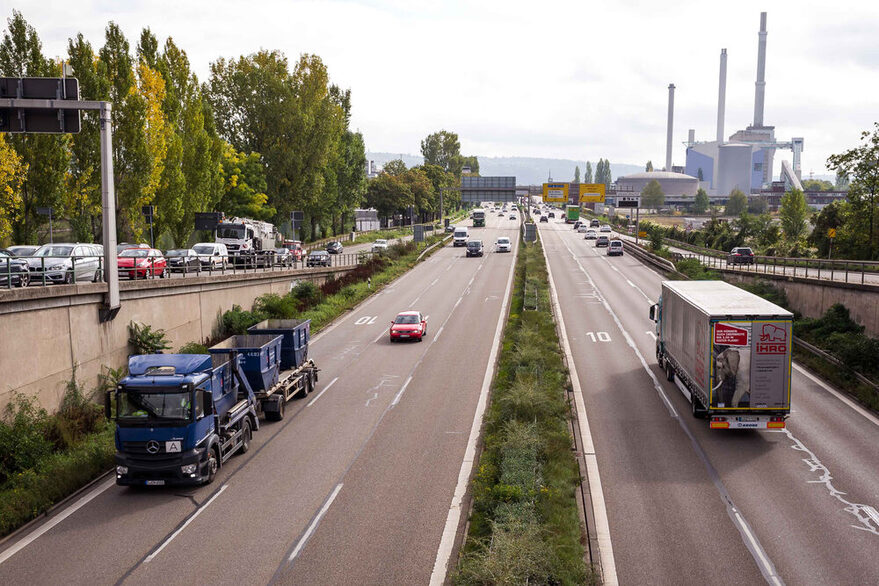 Blick auf eine Bundesstraße mit vielen Autos und Lastwagen. Links im Hintergrund ein große Fabrikhalle.