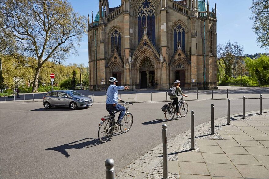 Zwei Fahrradfahrer biegen vor einem Auto ab, einer gibt ein Handzeichen.