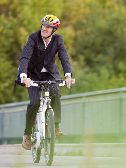 Geschäftsmann mit Anzug fährt mit einem Fahrrad über eine Brücke.