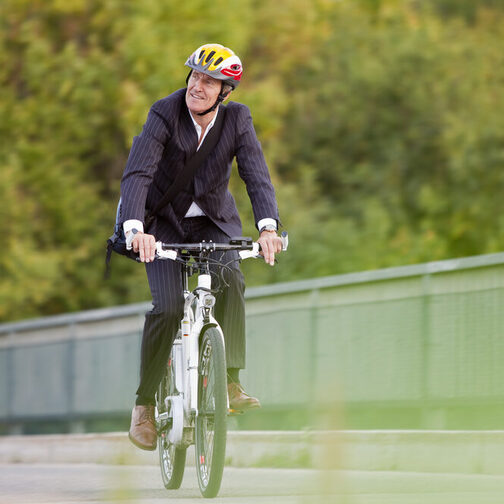 Geschäftsmann mit Anzug fährt mit einem Fahrrad über eine Brücke.