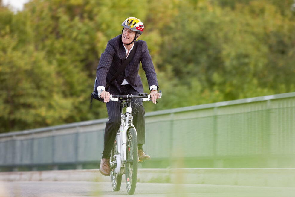 Geschäftsmann mit Anzug fährt mit einem Fahrrad über eine Brücke.