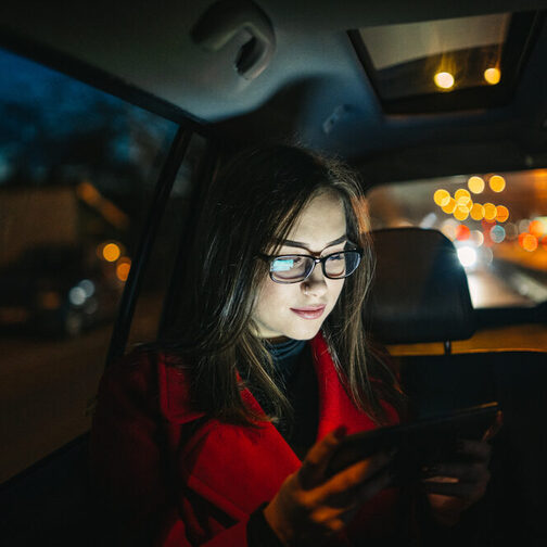 Eine junge Frau sitzt nachts in einem Taxi und schaut auf ihr Handy.