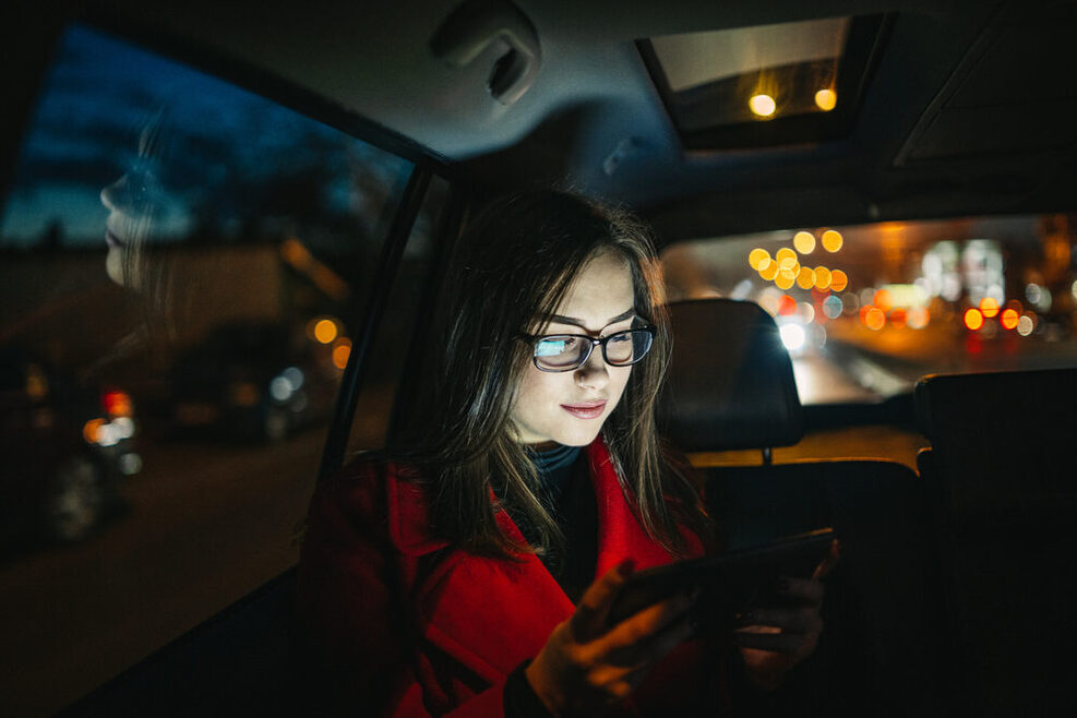 Eine junge Frau sitzt nachts in einem Taxi und schaut auf ihr Handy.