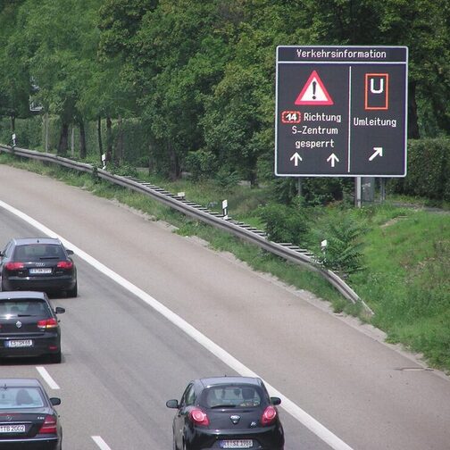 Autofahrer fahren an einer Variotafel vorbei in Richtung Zentrum.