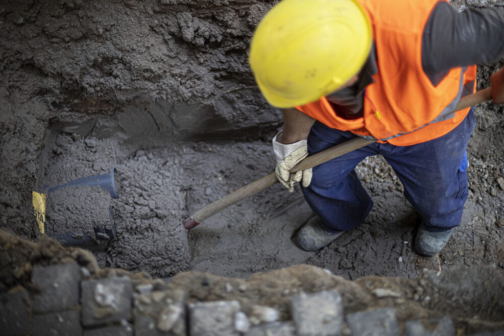 Ein Bauarbeiter steht in einer Grube und arbeitet mit einer Schaufel.