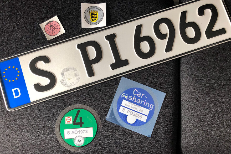 Auf einem Stuhl liegt ein Nummernschild und verschiedene Plaketten.