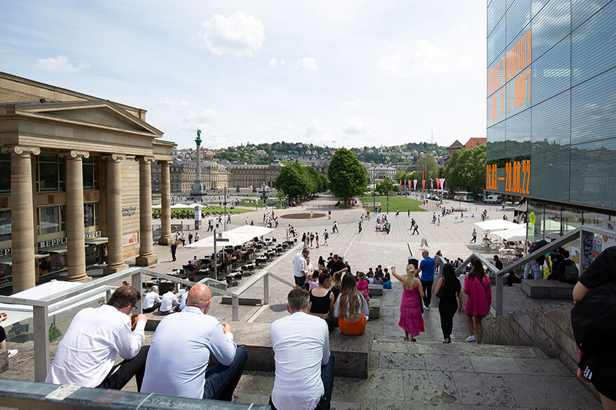 Blick von der Treppe am kleinen Schlossplatz auf die Königstraße und den Schlossplatz. Auf der Treppe sitzen Menschen.