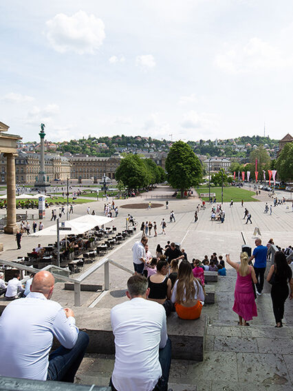 Blick von der Treppe am kleinen Schlossplatz auf die Königstraße und den Schlossplatz. Auf der Treppe sitzen Menschen.
